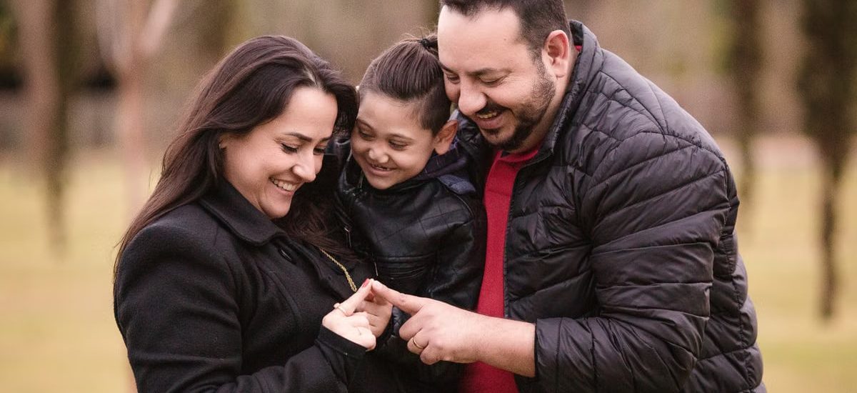 A joyful family of three enjoys a tender moment outdoors, depicting warmth and love.